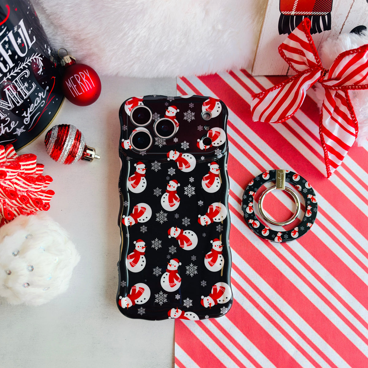 Snowman MagSafe grip ring beside the matching iPhone case, on candy cane stripes with a Santa hat and ornaments