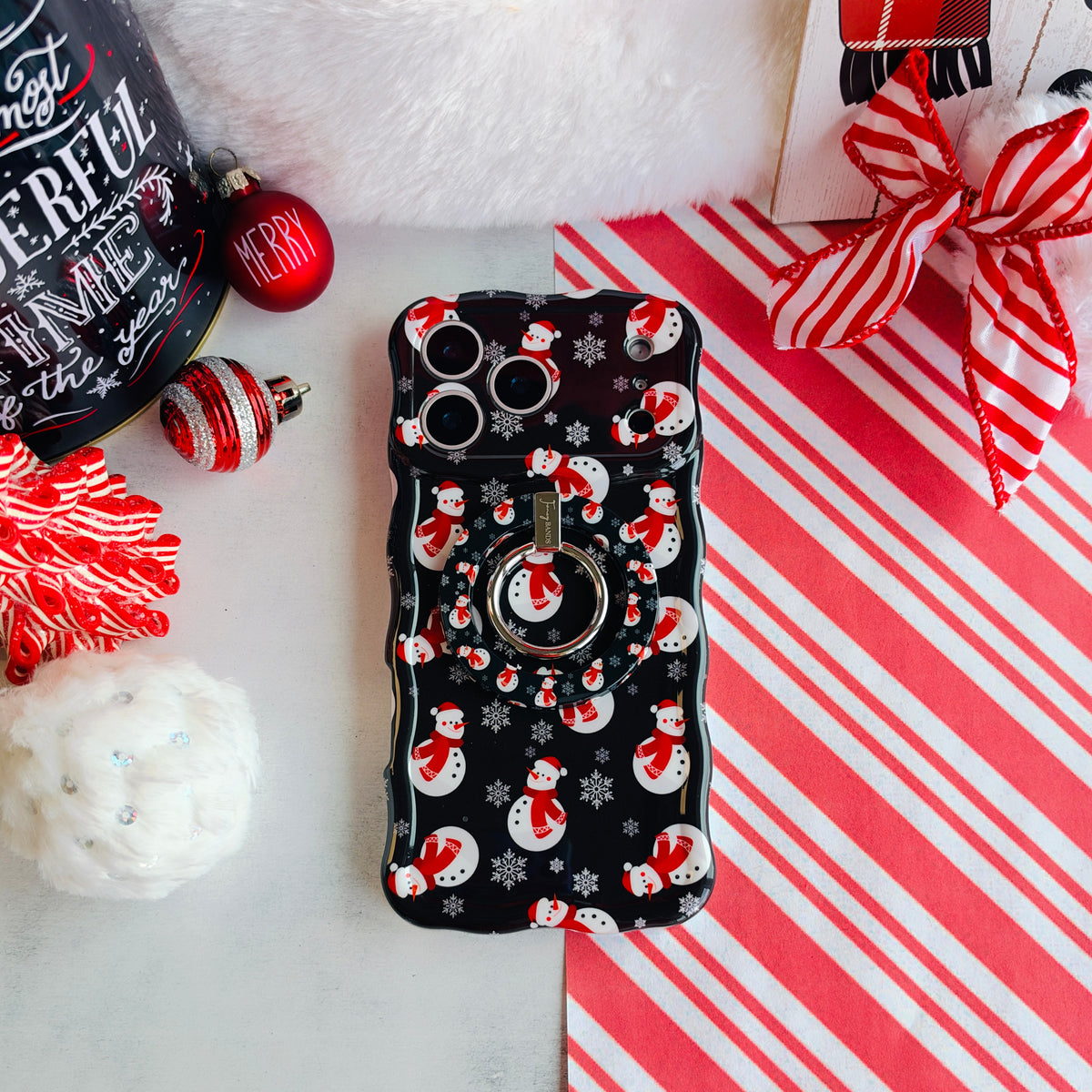 Snowman MagSafe grip ring attached to the matching iPhone case, on candy cane stripes with a Santa hat and ornaments