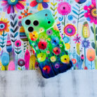 Wavy iPhone case featuring vibrant watercolor flowers in pink, red, yellow, and orange on a green and blue gradient background.