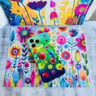 Wavy iPhone case featuring vibrant watercolor flowers in pink, red, yellow, and orange on a green and blue gradient background.