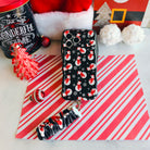 Snowman iPhone case with the matching scrunchie phone wrist strap attached, laid flat on candy cane stripes with a Santa hat and ornaments
