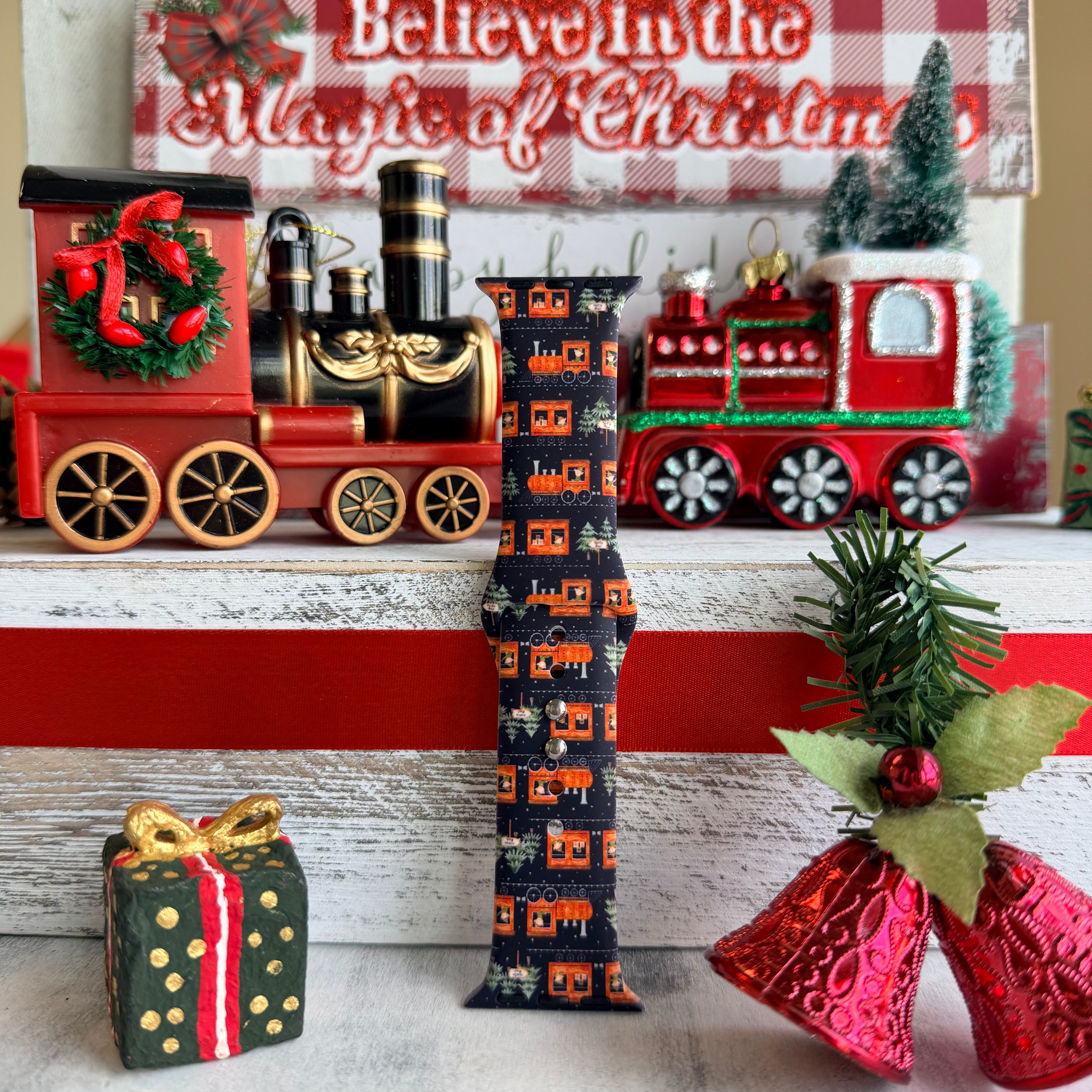 Decorative Christmas scene with a train, gift box, and bell on a wooden surface.