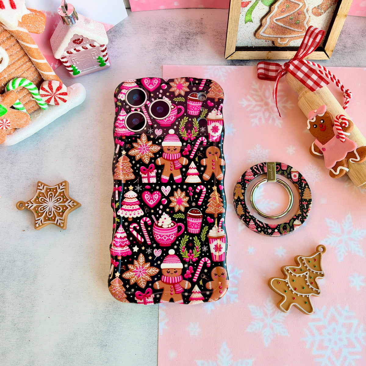 Merry Mugs & Ginger Hugs MagSafe grip ring beside the matching iPhone case, with gingerbread cookies and a gingerbread house