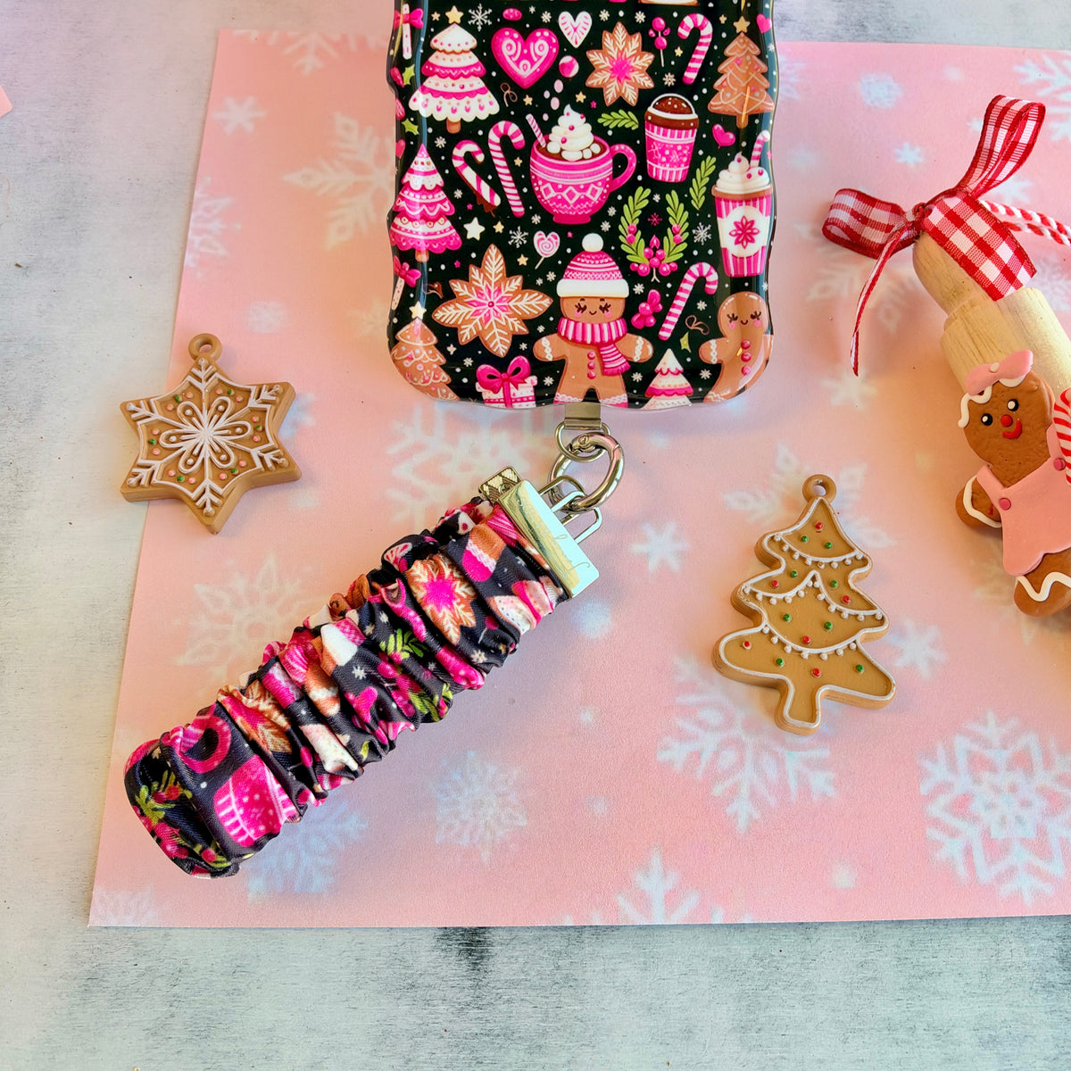 Merry Mugs & Ginger Hugs scrunchie phone wrist strap clipped to the matching iPhone case, with gingerbread cookies and a gingerbread house