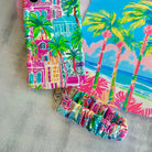 A vibrant La Palma Villa phone scrunchie wrist strap attached to a matching Wavy Luxe phone case with a colorful pink, green, and blue tropical palm tree print.