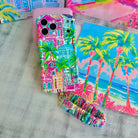 A vibrant La Palma Villa phone scrunchie wrist strap attached to a matching Wavy Luxe phone case with a colorful pink, green, and blue tropical palm tree print.