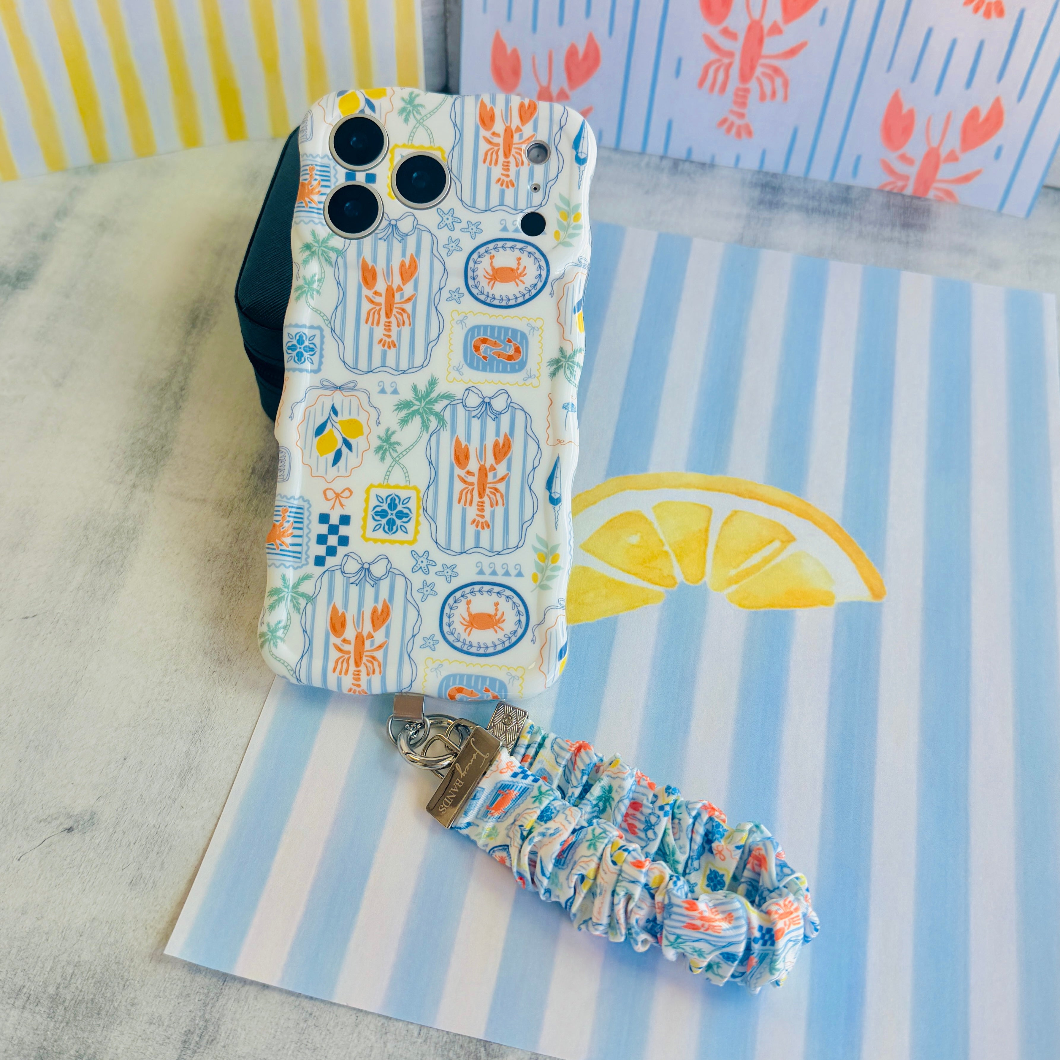 Coastal Catch scrunchie phone wrist strap clipped to the matching Coastal Catch Wavy Luxe iPhone case