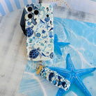 A Blue Lagoon scrunchie phone wrist strap with a blue and white sea turtle and ocean design attached to a matching Wavy Luxe case on a blue starfish background.