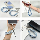 A Blue Lagoon scrunchie phone wrist strap with a blue and white sea turtle and ocean design attached to a matching Wavy Luxe case on a blue starfish background.