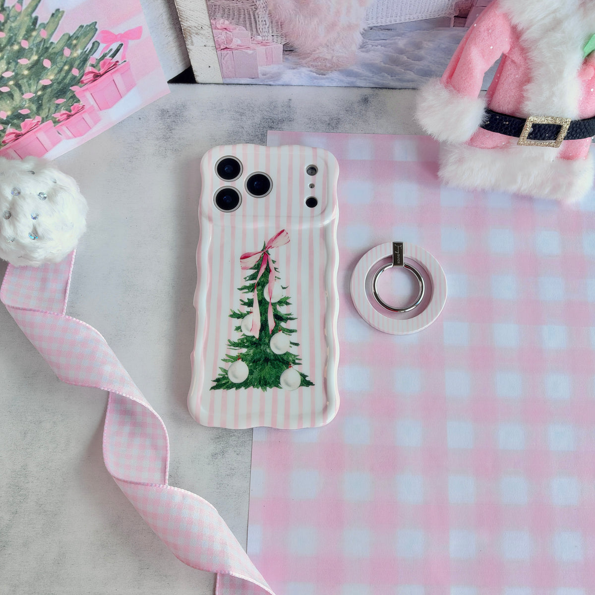 Pretty in PinkMas pink striped MagSafe grip ring beside the matching iPhone case, with pink gingham ribbon and a pink Santa coat