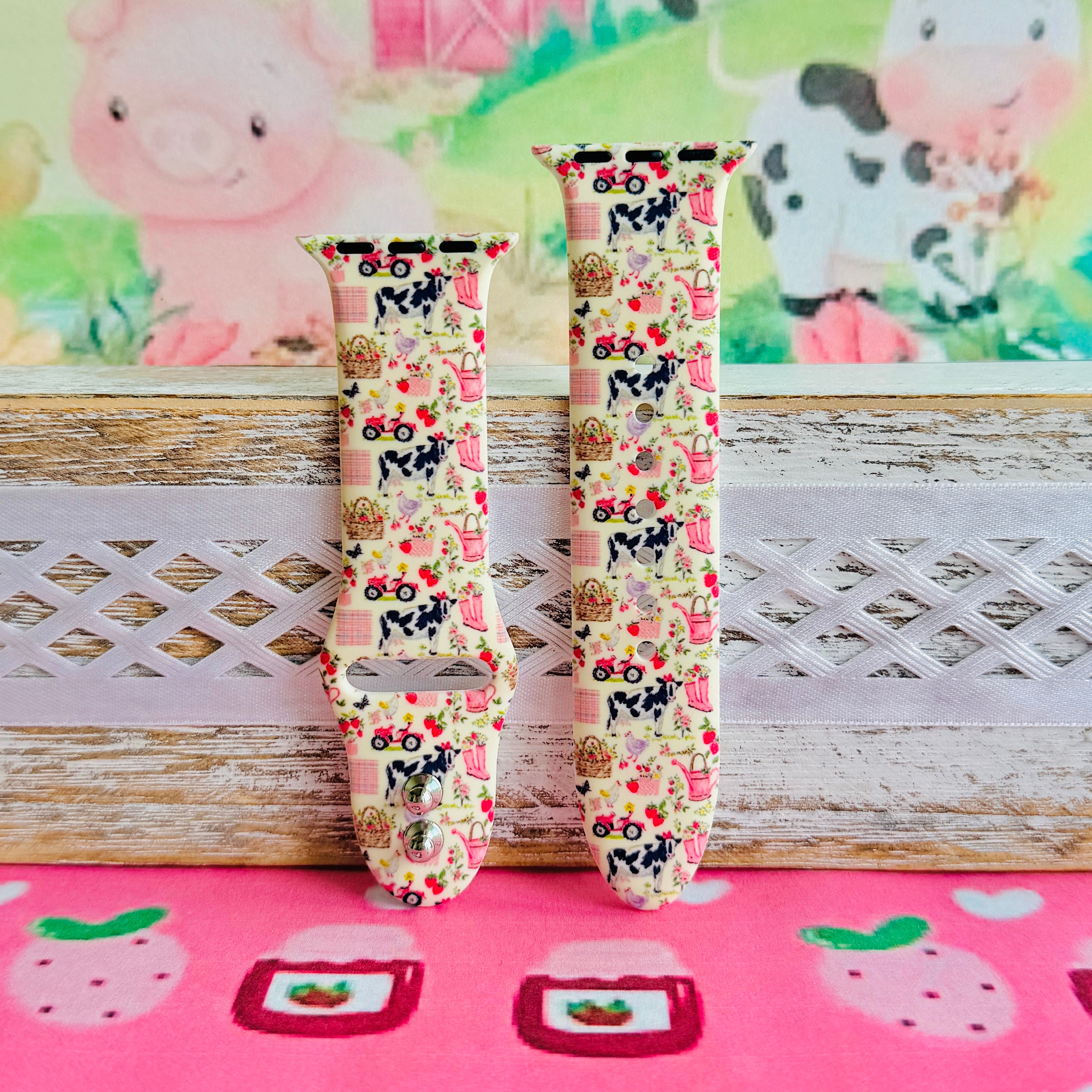 Farm Girl Cutie silicone Apple Watch band with dairy cows, red tractors, chickens, ducks, pink watering cans, strawberries, baskets, and roses on a cream base with pink gingham squares, shown displayed and worn on Apple Watch against a farmhouse country backdrop.