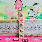 Farm Girl Cutie silicone Samsung Galaxy Watch band with dairy cows, red tractors, chickens, ducks, pink watering cans, strawberries, baskets, and roses on a cream base with pink gingham squares, shown displayed and worn against a farmhouse country backdrop.