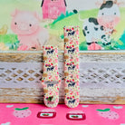Farm Girl Cutie silicone Samsung Galaxy Watch band with dairy cows, red tractors, chickens, ducks, pink watering cans, strawberries, baskets, and roses on a cream base with pink gingham squares, shown displayed and worn against a farmhouse country backdrop.