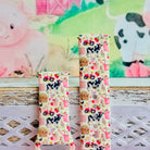 Farm Girl Cutie silicone Samsung Galaxy Watch band with dairy cows, red tractors, chickens, ducks, pink watering cans, strawberries, baskets, and roses on a cream base with pink gingham squares, shown displayed and worn against a farmhouse country backdrop.