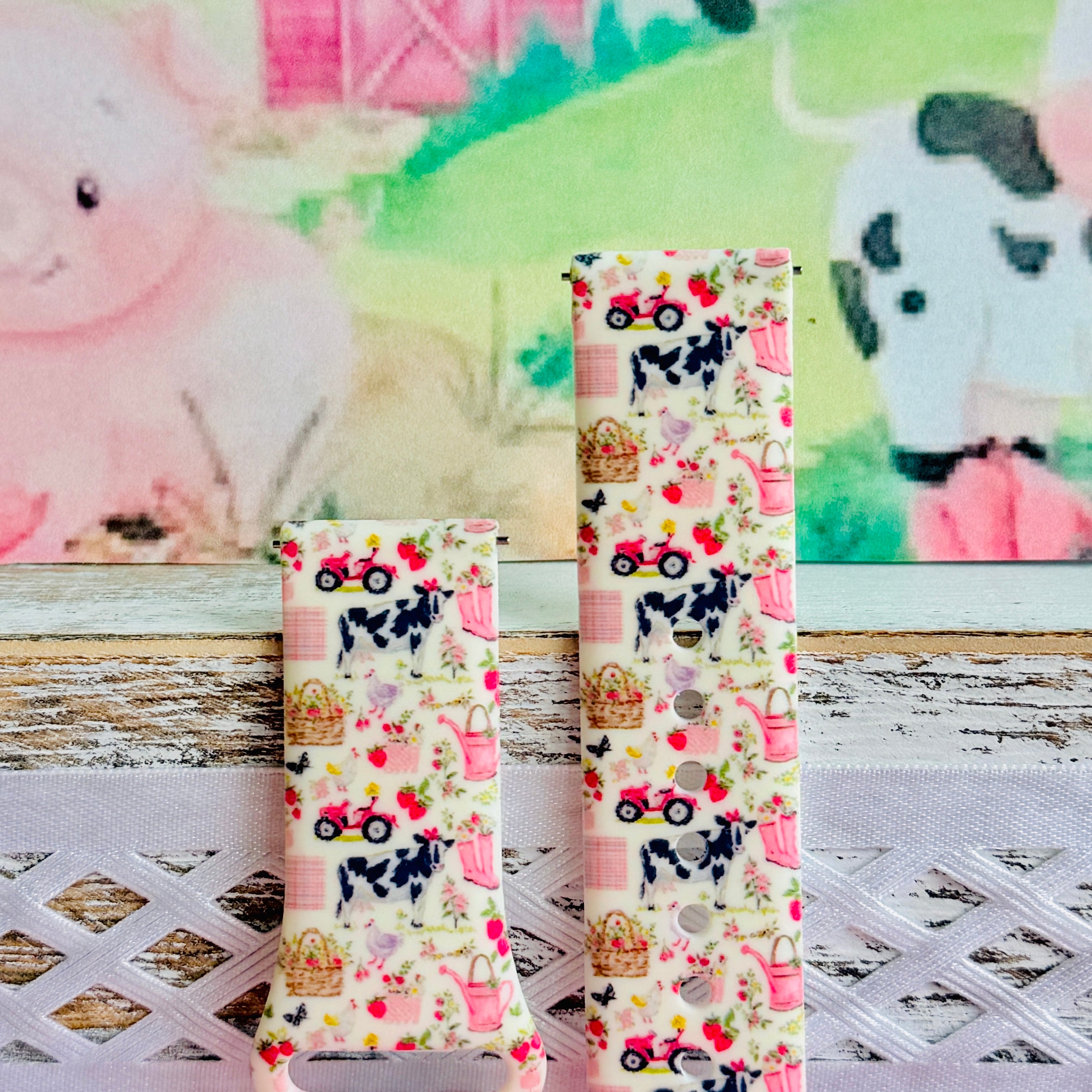 Farm Girl Cutie silicone Samsung Galaxy Watch band with dairy cows, red tractors, chickens, ducks, pink watering cans, strawberries, baskets, and roses on a cream base with pink gingham squares, shown displayed and worn against a farmhouse country backdrop.