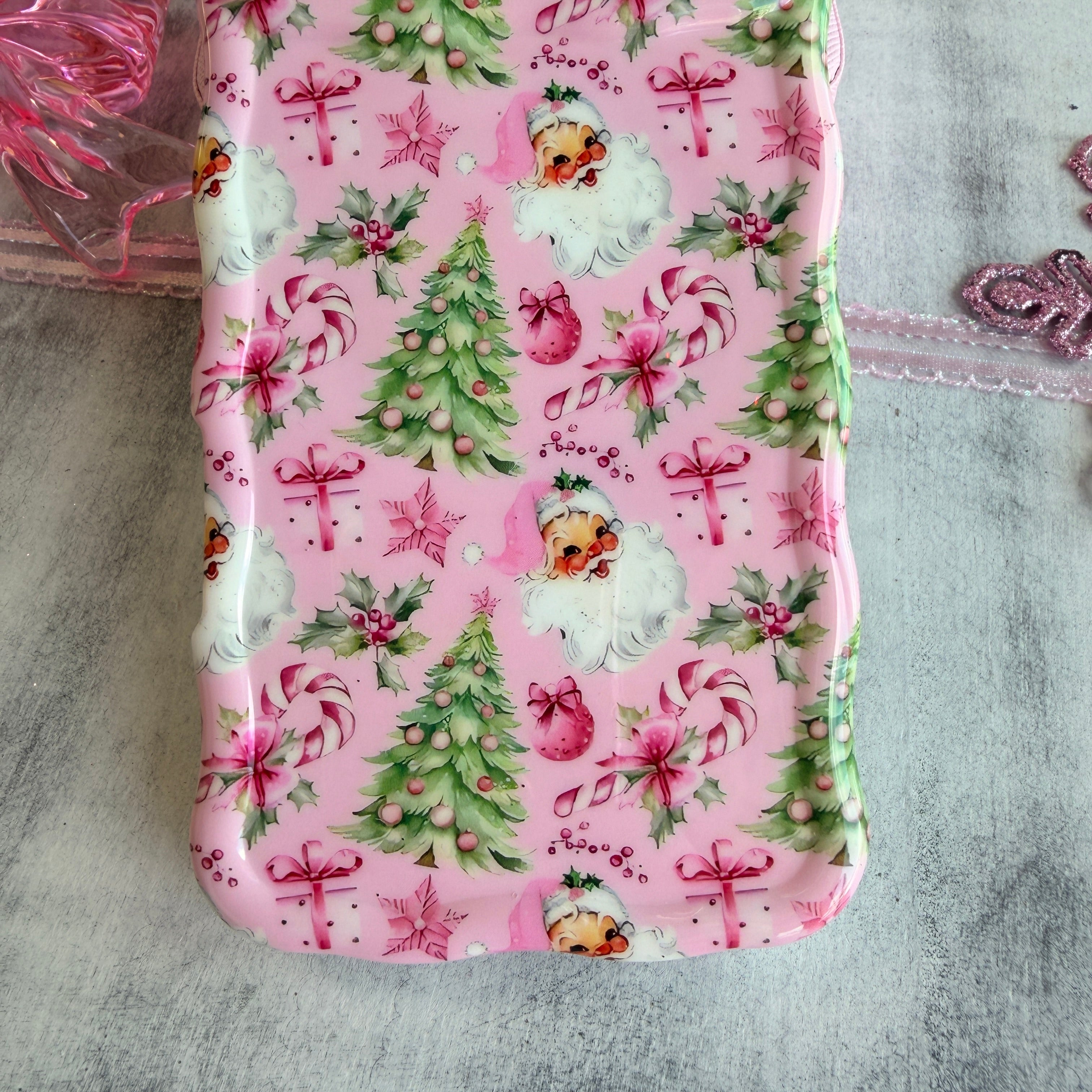 Pink phone case with Christmas-themed design featuring Santa Claus, trees, and presents on a textured surface.
