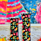 Bloom Bonita silicone Apple Watch band with Mexican folk art florals in coral, red, yellow, teal, and pink on a black base, shown displayed against a vibrant Mexican folk art backdrop with rose and dress accents.