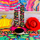 Bloom Bonita silicone Samsung Galaxy Watch band with Mexican folk art florals in coral, red, yellow, teal, and pink on a black base, shown displayed against a vibrant Mexican folk art backdrop with rose and dress accents.