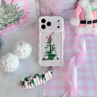 Pretty in PinkMas iPhone case with the matching scrunchie phone wrist strap attached, laid flat beside a pink Santa coat