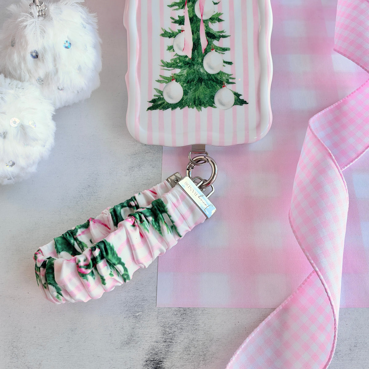 Pretty in PinkMas scrunchie phone wrist strap clipped to the matching iPhone case, with white pom-poms and pink gingham ribbon