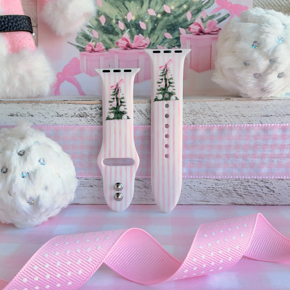 Pretty in PinkMas Apple Watch band straps with pink polka-dot ribbon and white pom-poms on a whitewashed shelf