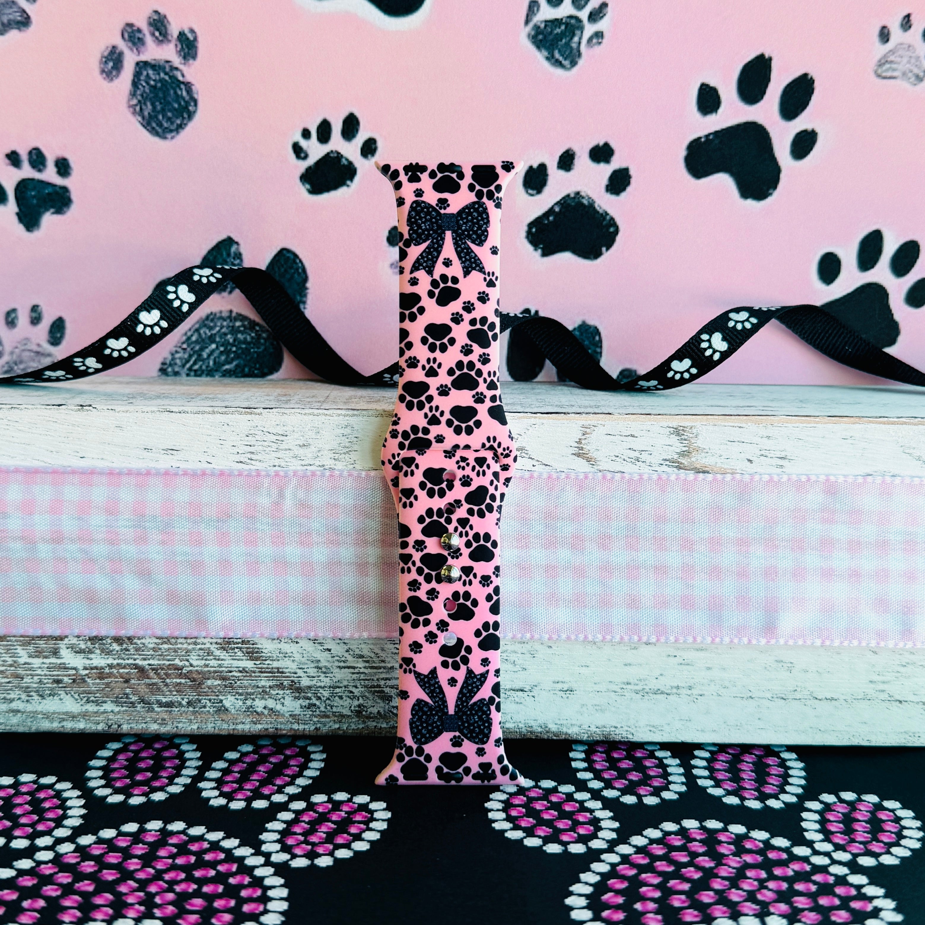 Pretty Little Paws Apple Watch band with black paw prints and polka dot bow on pink background with paw decorations
