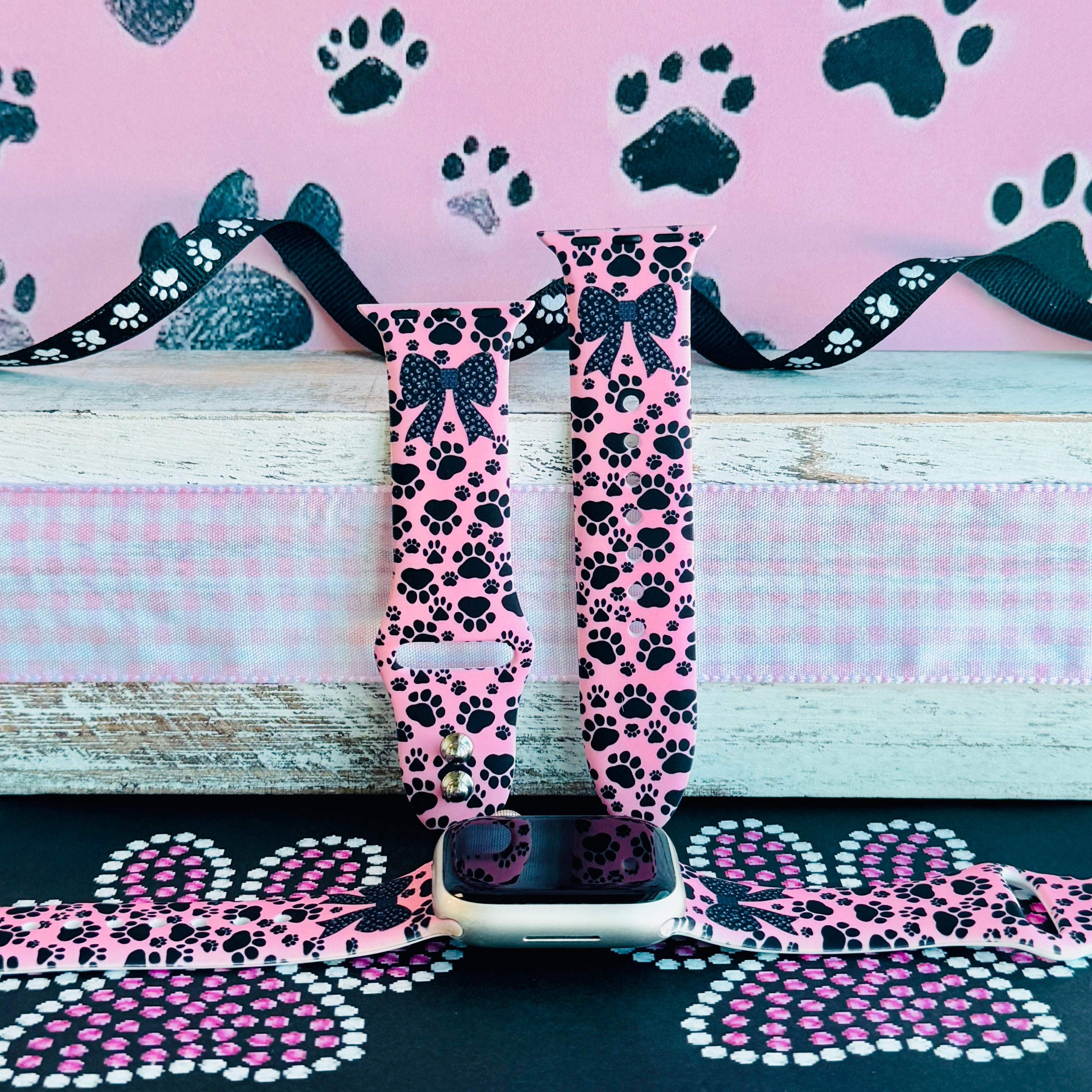 Pretty Little Paws Apple Watch band with black paw prints and polka dot bow on pink background with paw decorations
