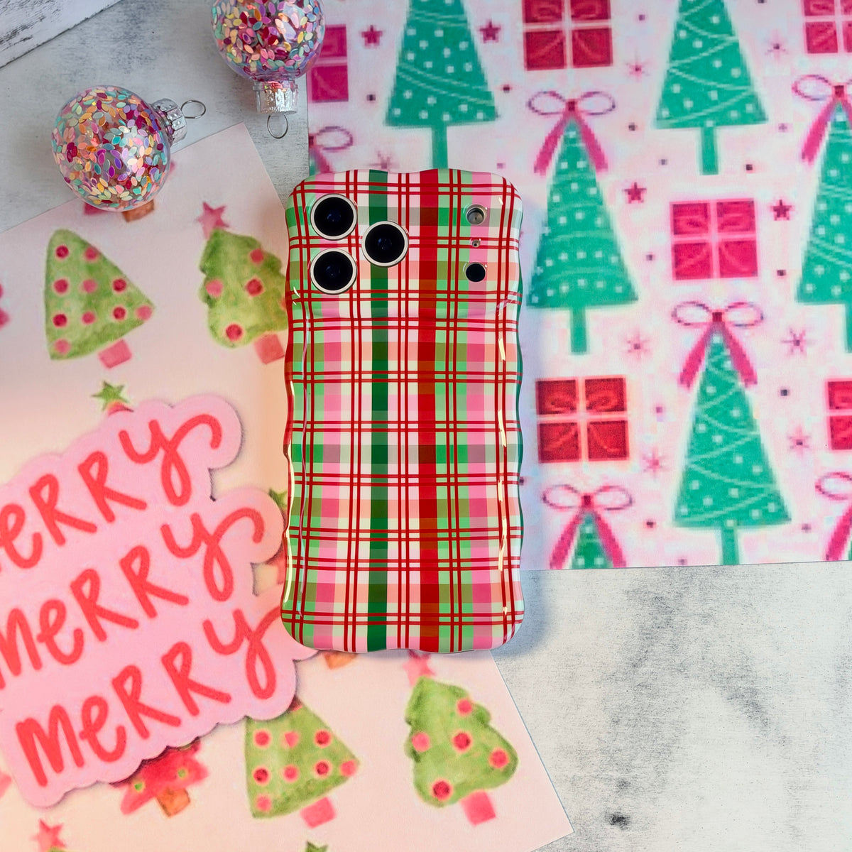 Merry Little Plaid iPhone case lying on pink and mint Christmas tree wrapping paper
