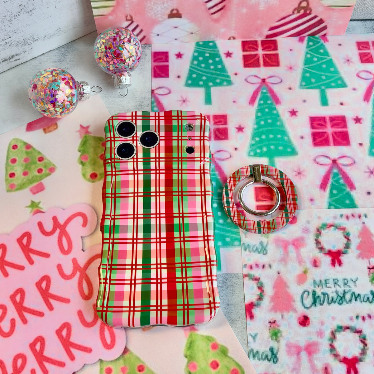 Merry Little Plaid MagSafe grip ring beside the matching iPhone case on pink and mint Christmas wrapping paper