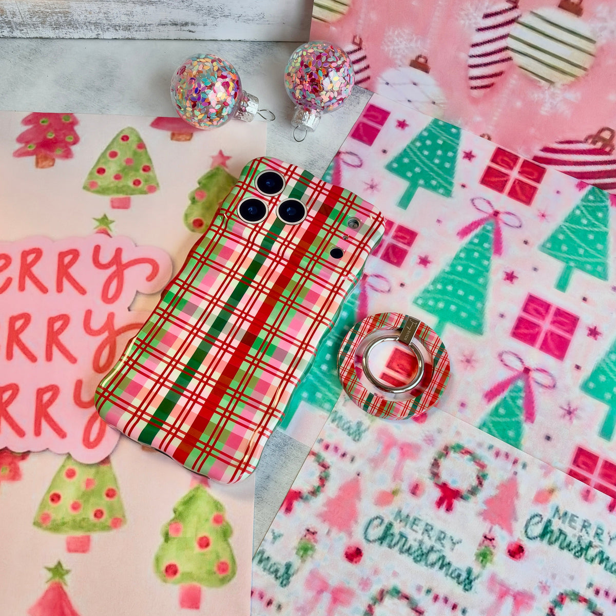 Merry Little Plaid Hold It Fancy MagSafe grip ring snapped onto the matching plaid iPhone case, on a pink and mint Christmas tree backdrop