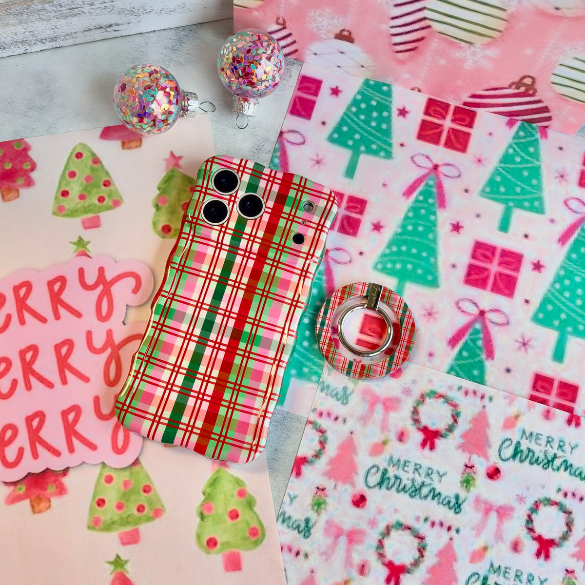 Merry Little Plaid iPhone case with the matching plaid grip ring set beside it, with a pink Merry sign and glitter ornaments