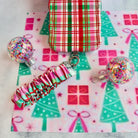 Merry Little Plaid scrunchie phone wrist strap clipped to the matching iPhone case, with glitter ornaments on Christmas tree paper