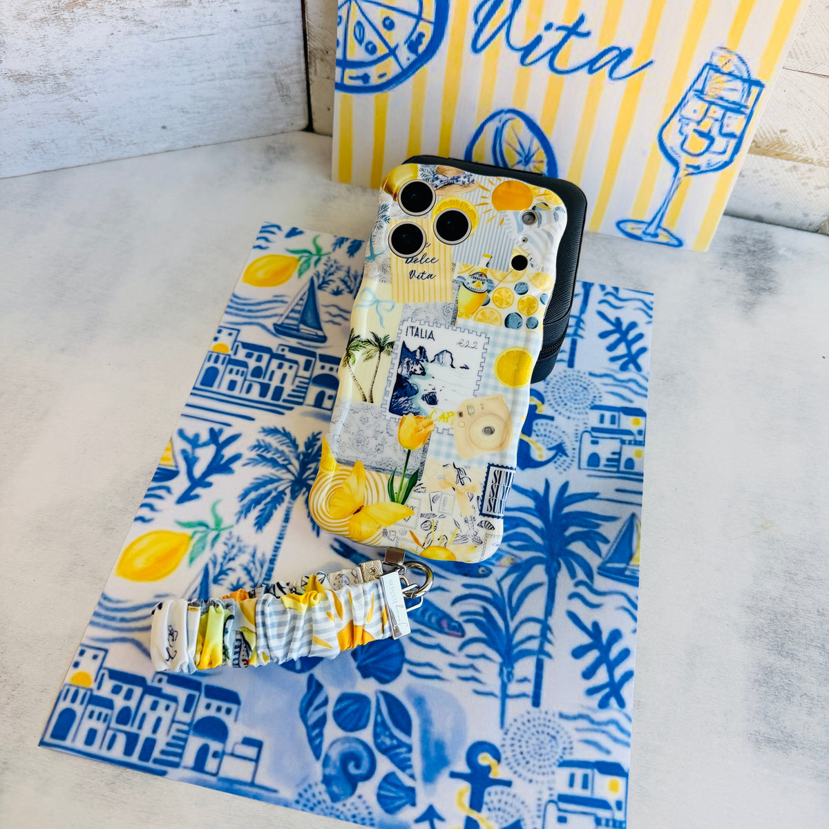 La Dolce Summer scrunchie phone wrist strap laid out with the matching Mediterranean lemon Wavy Luxe iPhone case