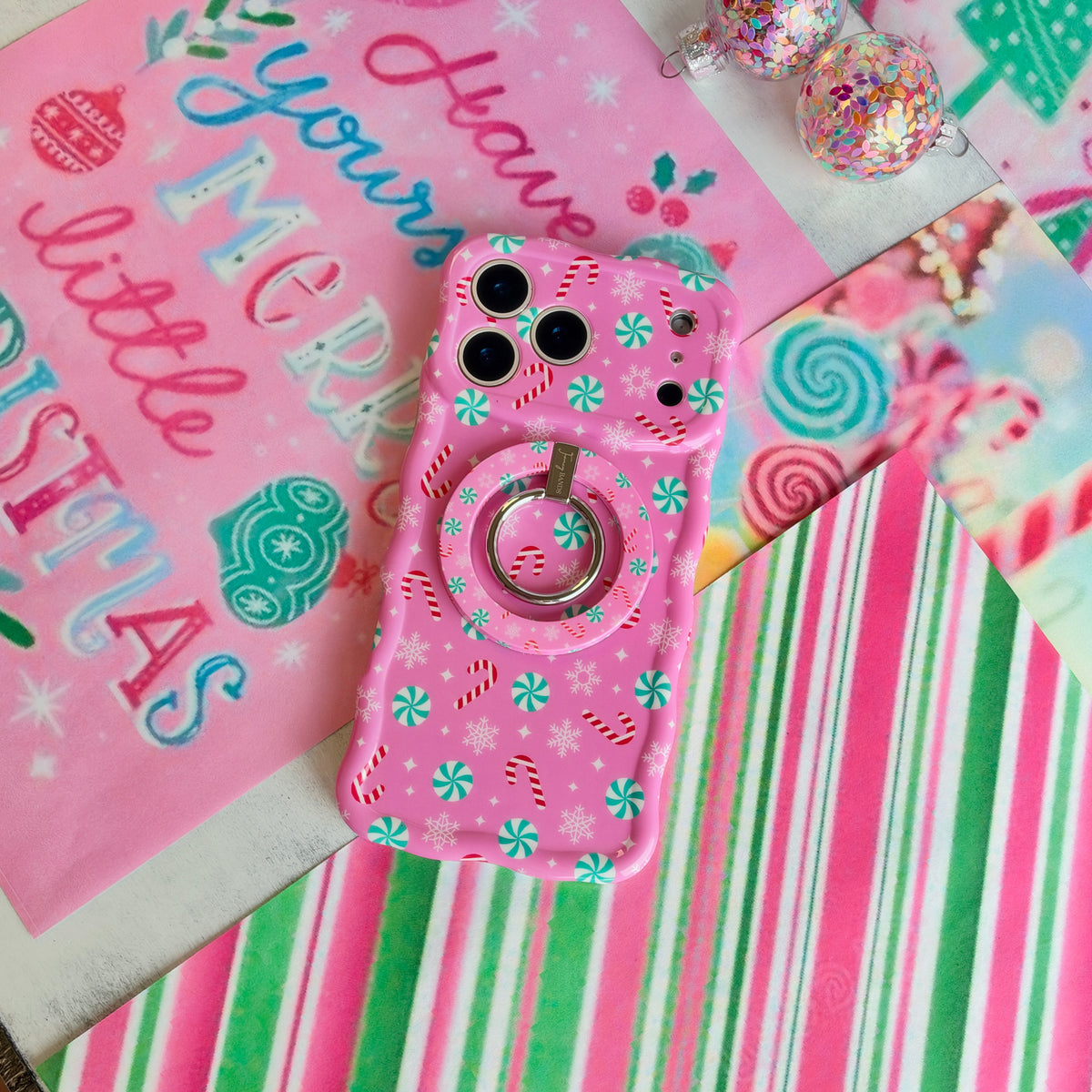 Peppermint Cutie iPhone case with the matching pink peppermint MagSafe grip ring snapped on, on candy stripe paper
