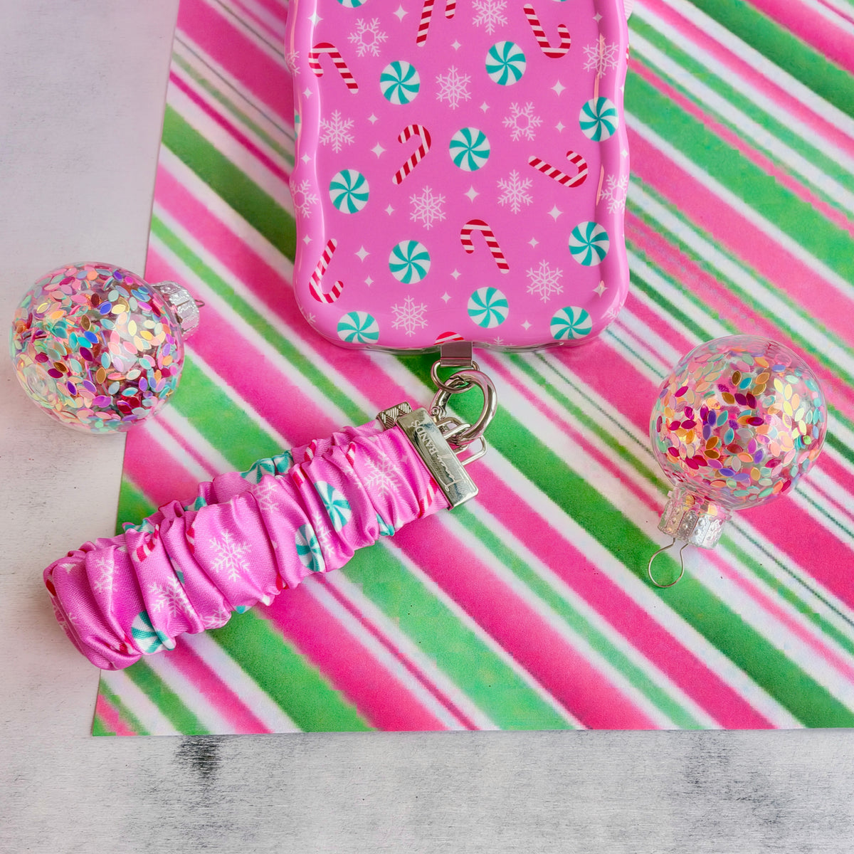 Peppermint Cutie scrunchie phone wrist strap clipped to the matching iPhone case on candy stripe paper with glitter ornaments