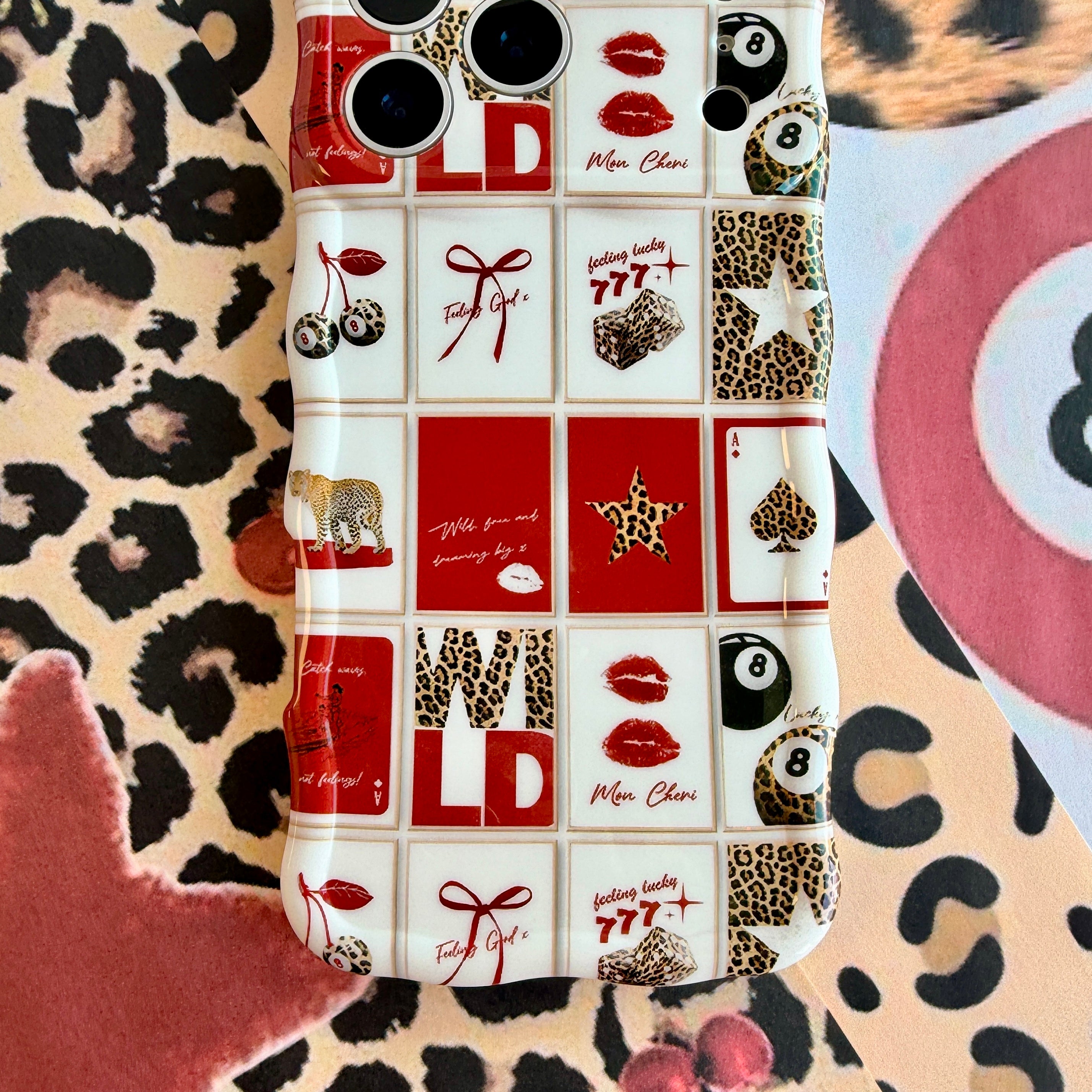 Trendy red and white wavy iPhone case featuring a collage of leopard print cherries, 8-balls, red lips, and lucky 777 dice with a high-gloss finish.