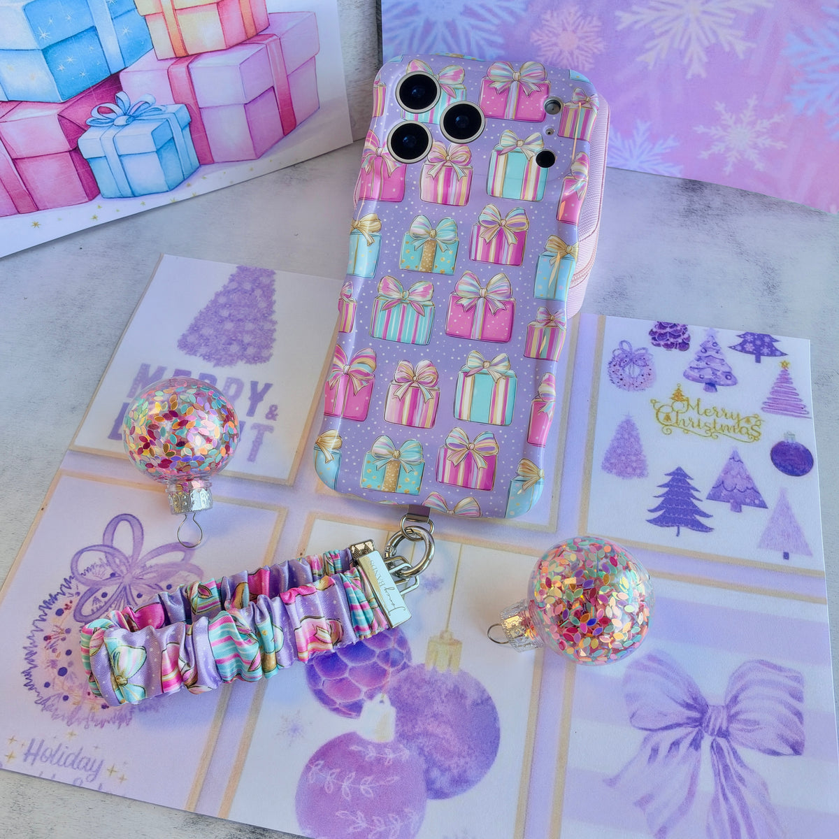 Flat lay of the No Peeking, Darling iPhone case with its pastel present scrunchie wrist strap and confetti glitter ornaments