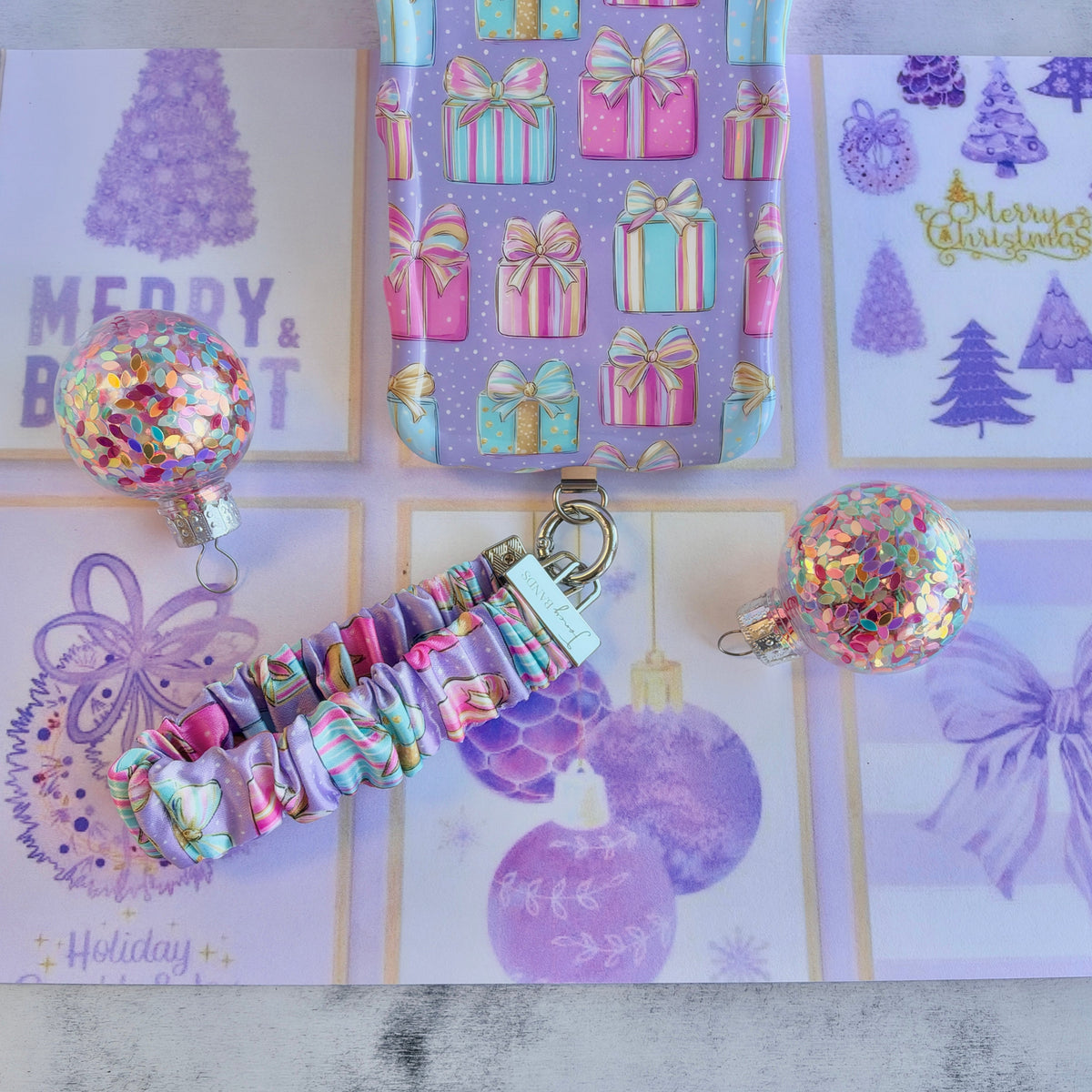 No Peeking, Darling scrunchie phone wrist strap clipped below the matching pastel present iPhone case among glitter ornaments