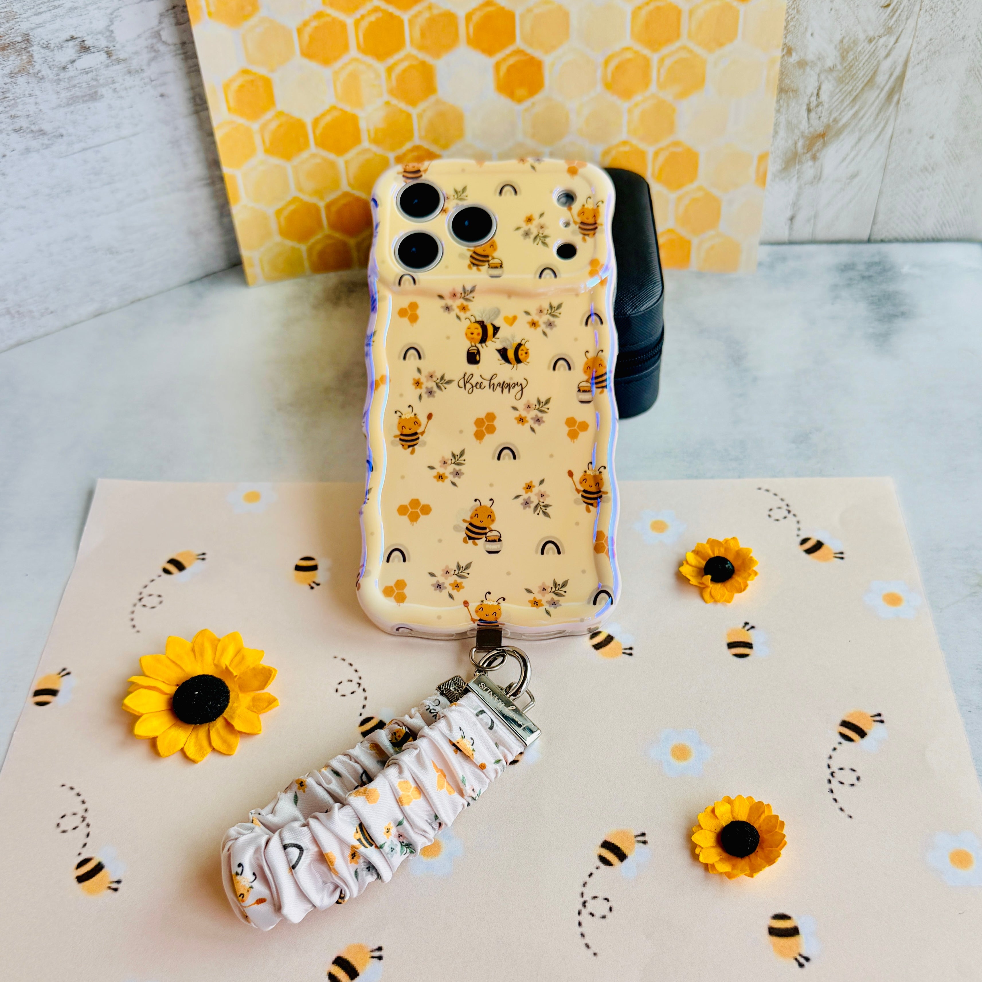 Bee Happy scrunchie phone wrist strap clipped to the matching Bee Happy Wavy Luxe iPhone case