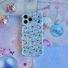 Twinkle All The Way iPhone case lying flat beside a hanging blue glass ornament and glitter baubles
