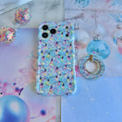 Twinkle All The Way Christmas lights iPhone case lying flat with its matching MagSafe grip ring and a blue glass ornament