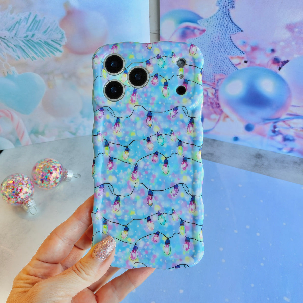 Hand holding the Twinkle All The Way Wavy Luxe MagSafe iPhone case, strands of pink, violet, aqua and lime Christmas lights on pastel blue