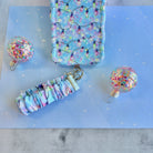 Twinkle All The Way scrunchie phone wrist strap clipped below the matching iPhone case between two glitter ornaments