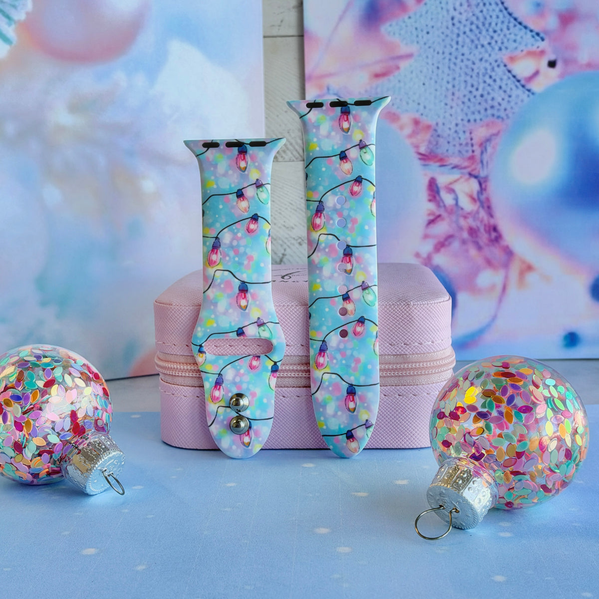 Both straps of the Twinkle All The Way silicone Apple Watch band propped on a pink jewelry box with glitter ornaments