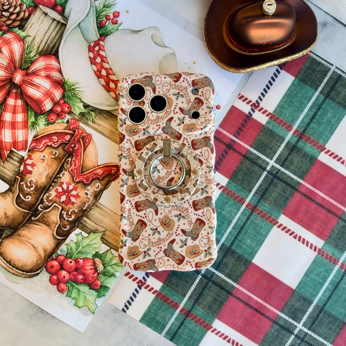 Close-up of the Boot Scootin' Christmas MagSafe grip ring on the matching cowboy boot iPhone case, on red and green plaid