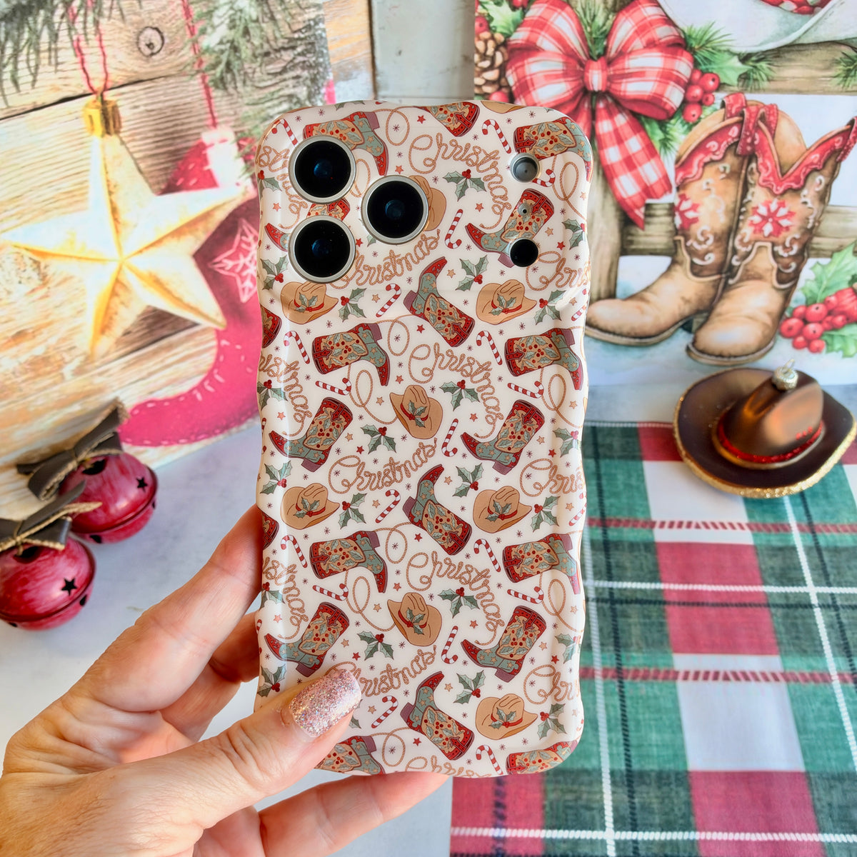 Hand holding the Boot Scootin' Christmas Wavy Luxe MagSafe iPhone case, cowboy boots, hats and lasso Christmas lettering on cream, beside a gold star and cowboy boot art
