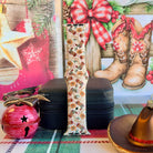 Boot Scootin' Christmas Apple Watch band buckled and standing on a black jewelry box between a red jingle bell and a cowboy hat ornament