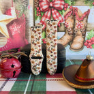 Both straps of the Boot Scootin' Christmas silicone Apple Watch band on a black jewelry box with a red jingle bell and cowboy hat ornament