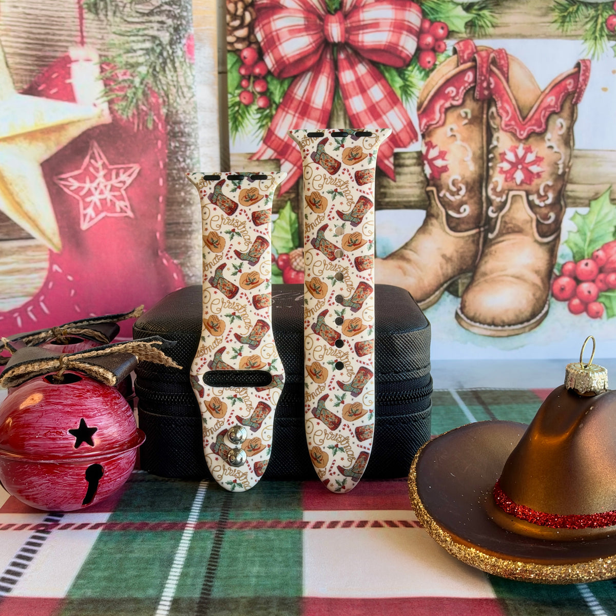 Both straps of the Boot Scootin' Christmas silicone Apple Watch band on a black jewelry box with a red jingle bell and cowboy hat ornament