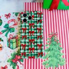 Plaid Tidings & Bows iPhone case lying flat on red and white striped paper beside a watercolor Christmas tree